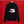 A black pullover Scroggin hoodie hanging on a wooden hanger against a solid red background. The back of the hoodie features a white line-art graphic of a greenhouse.