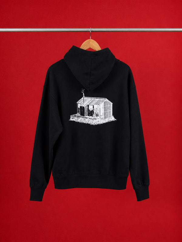 A black pullover Scroggin hoodie hanging on a wooden hanger against a solid red background. The back of the hoodie features a white line-art graphic of a greenhouse.